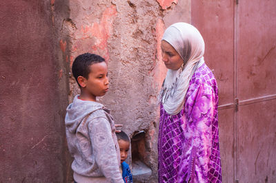 Side view of siblings standing against wall