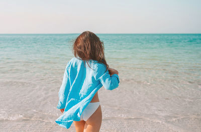 Rear view of boy standing on beach against sky