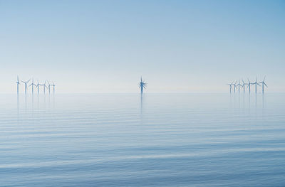 View of wind farm turbines in sun rise haze across still ocean tranquil new energy production