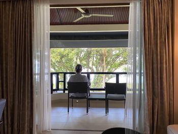 Rear view of man sitting on chair against window