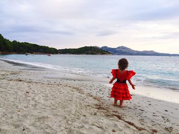 Rear view of girl on beach against sky