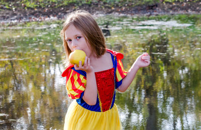 A young girl enjoys a fresh apple, as she plays dress up in her princess halloween costume.