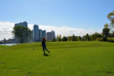 Full length of woman on field against sky in city during sunny day