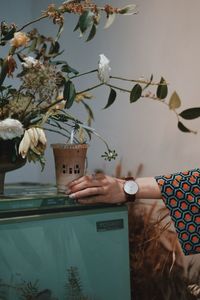 Midsection of person by flower vase on table