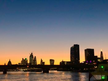 River by illuminated buildings against sky during sunset