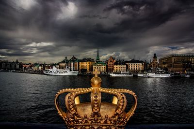 View of city at waterfront against cloudy sky