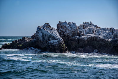 Rocks by sea against clear blue sky