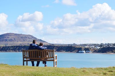 Rear view of couple sitting on bench in front of lake