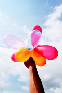 Low angle view of hand holding colorful balloons against sky