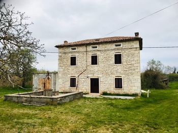 Old building by trees on field against sky