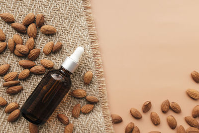 Almond essential oil in glass bottle, raw almond kernels. cosmetic concept on beige background