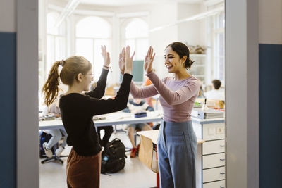 Smiling female teacher giving high-five to girl standing in classroom