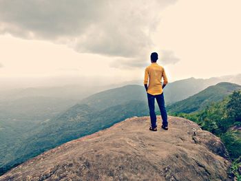 Rear view of man standing on mountain against sky