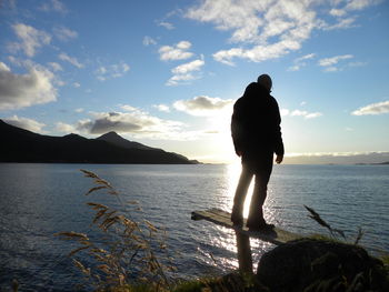Rear view of silhouette man standing by sea against sky