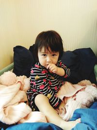 Portrait of cute baby girl sitting on bed at home
