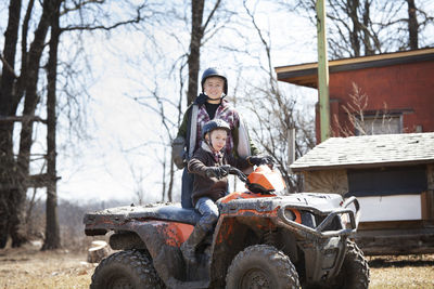 Portrait of boy sitting on quadbike while brother standing on field