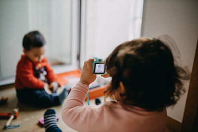 Rear view of sister taking pictures of her brother