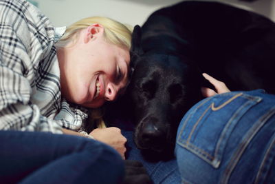 Young woman smiling while lying by black labrador on bed