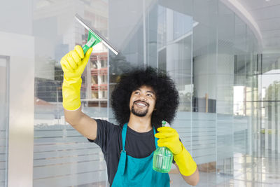 Smiling young man cleaning window in office