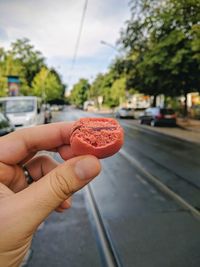 Close-up of woman holding red macaroon on road in city