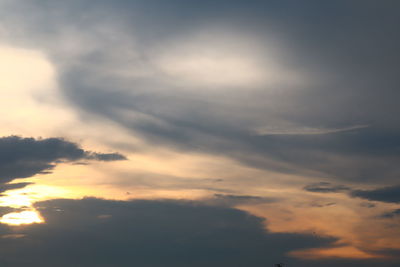 Low angle view of sunlight streaming through clouds during sunset