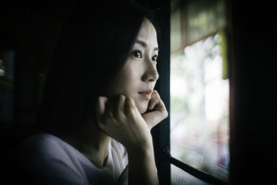 Close-up of woman looking through window at home