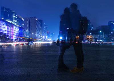 Woman standing on illuminated city street at night