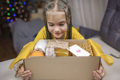 Girl packing care box with tea, honey, cookies and knitted wool socks for grandmother on christmas