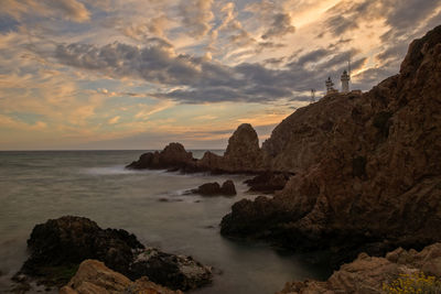 Rocks on beach against sky during sunset