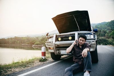 Man sitting by car on road