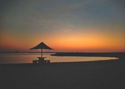 Silhouette beach by sea against sky during sunset