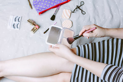 High angle view of woman with beauty products sitting on bed at home