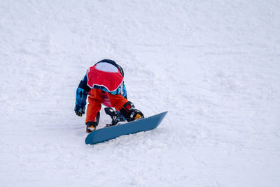 Person with snowboard on the snow. one asian child is falling on the ground. winter sport.