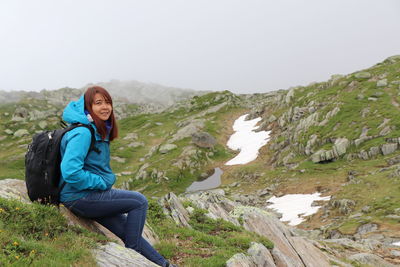 Portrait of young woman sitting on rock against mountains