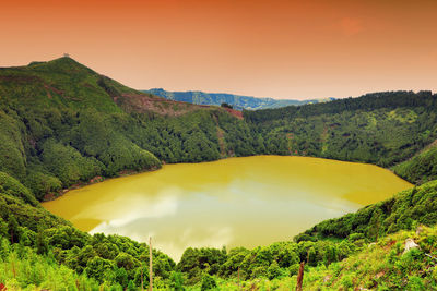 Scenic view of lake amidst mountains against orange sky at azores