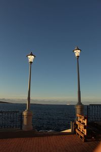 Street light by sea against clear sky during sunset