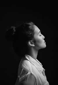 Side view of young woman against black background