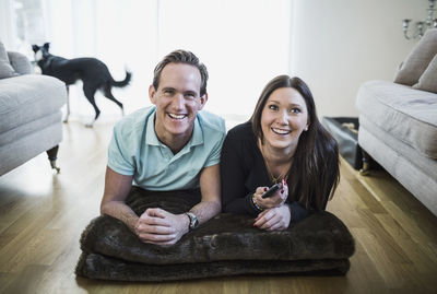 Happy couple watching tv while lying on floor in living room