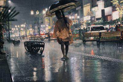 Rear view of woman walking on wet road at night