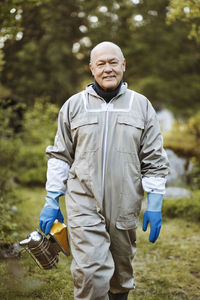 Portrait of happy beekeeper holding smoker while walking on field