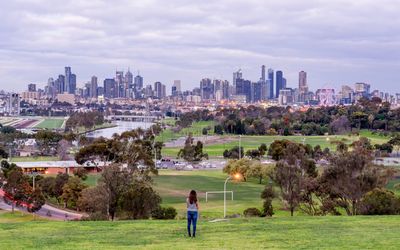 Rear view of woman standing while looking at city against cloudy sky