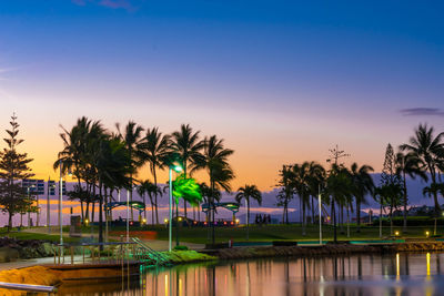 Palm trees by swimming pool against sky during sunset