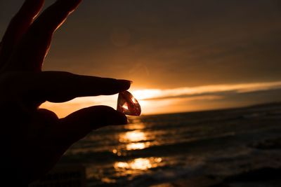 Cropped hand of woman holding diamond against sea at sunset