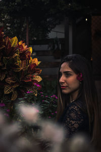 Portrait of young woman standing by flowering plants