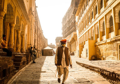 Rear view of man walking on cobblestone street amidst buildings in city