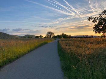 Empty road amidst field against sky during sunset