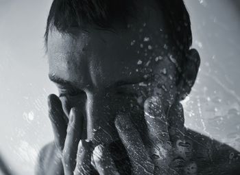 Close-up of depressed young man seen through wet glass