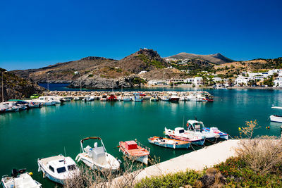 Boats moored in harbor against clear blue sky