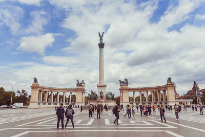 Group of people in front of historical building against cloudy sky