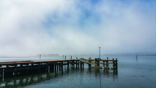 Weathered wooden pier in bay against foggy sky